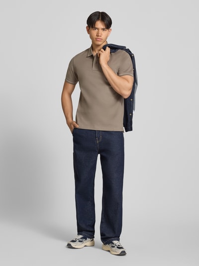 Männermodel trägt Regular Fit Poloshirt aus reiner Baumwolle von Tommy Jeans in Unifarben mit Logo-Stitching, Ganzkörperansicht von vorne.