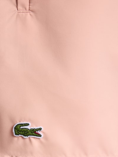 Produktfoto, Badeshorts mit Logo-Stitching von Lacoste in unifarbenem Rosa mit grünem Krokodil, glatte Textur, Detailaufnahme.
