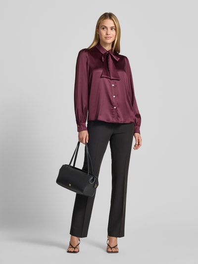Vrouwenmodel draagt Regular Fit Hemdbluse aus Satin van Christian Berg Woman Selection in bordeaux, met overhemdkraag en sierstrik, lange mouwen, gladde satijnen textuur, gecombineerd met zwarte broek, voorkant volledig zicht.