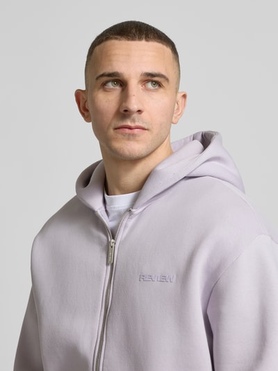 Männermodel trägt Sweatjacke mit Känguru-Tasche von REVIEW in hellem Fliederton, Baumwoll-Mix, Relaxed Fit, Nahaufnahme Oberkörper.