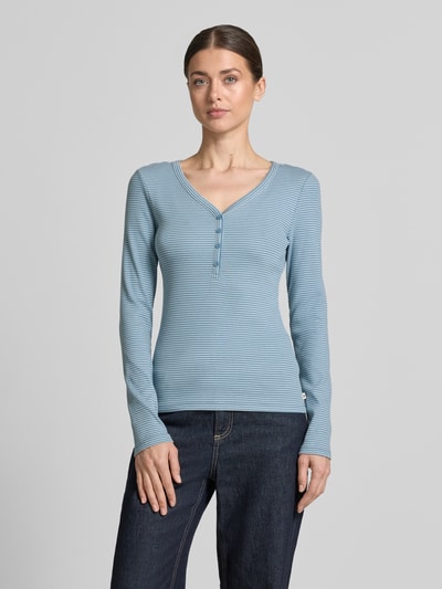 Modelka nosi Regular Fit Langarmshirt mit Henley-Ausschnitt von Tom Tailor Denim, efekt: jednolity kolor, krój: krój regular fit, dekolt: dekolt henley, rękaw: długi rękaw, materiał: mieszanka bawełny, jasnoniebieski odcień, delikatna prążkowana faktura, całkowite ujęcie z przodu.
