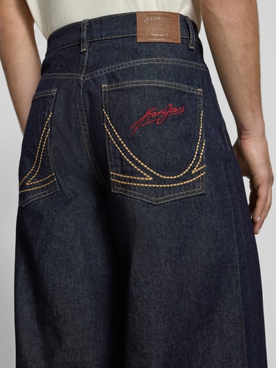 Männermodel trägt Wide Fit Jeans mit Logo-Stitching von KARL KANI, tiefblau, markante gelbe Nähte, reine Baumwolle, Nahaufnahme Rückansicht.
