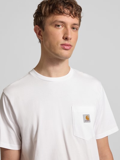 Männermodel trägt Regular Fit T-Shirt mit Logo-Patch von Carhartt Work In Progress in Weiß, reine Baumwolle, Brusttasche, Nahaufnahme Oberkörper.