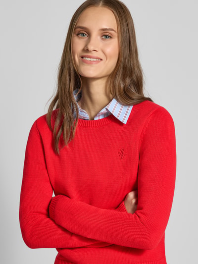 Frauenmodel trägt Slim Fit Pullover aus reiner Baumwolle von REVIEW in kräftigem Rot, Strick-Optik, Logo-Stitching, Nahaufnahme Oberkörper.