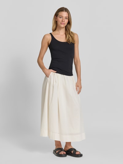 Modelka kobieca ma na sobie Slim Fit Top mit Rundhalsausschnitt von Jake*s Casual z mieszanki bawełny, krój slim fit, okrągły dekolt, bez rękawów, długość tyłu w rozmiarze S: 45 cm, czarny top, biała rozkloszowana spódnica, ciemne sandały, gładkie tło, pełny widok sylwetki z przodu.