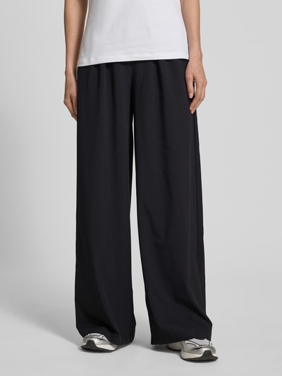 Frauenmodel trägt Wide Fit Pants mit elastischem Bund Modell 'SELENE' von Guess Activewear, schwarzer Stoff, Ganzkörperansicht von vorne.