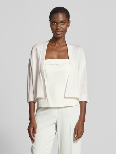 Modelka nosi kardigan rozpinany 'Strickjacke aus Lyocell-Baumwoll-Mix in offener Passform' od comma, mieszanka lyocellu i bawełny, krój regular fit, otwarty fason, rękaw o dł. 3/4, długość tyłu w rozmiarze S: 43 cm, długość rękawa w rozmiarze S: 32 cm, jasny kolor, gładka faktura, widok całej sylwetki z przodu.