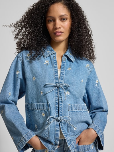 Vrouwenmodel draagt Jeansjacke mit Stitchings und Schnürung van Jake*s Casual, relaxed fit, bloemenstiksels, striksluiting, opgestikte zakken, blauwe denim, overhemdkraag, voorkant, close-up bovenlichaam.