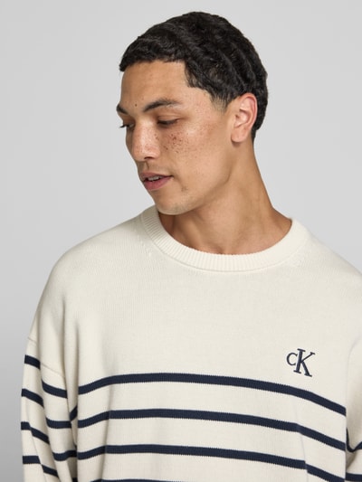 Männermodel trägt Regular Fit Strickpullover aus reiner Baumwolle von Calvin Klein Jeans met gebreide look, gestreept motief, gestikt logo, ronde hals, lange mouw, rompzoom geribd, puur katoen materiaal. Nahaufnahme Oberkörper.