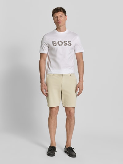 Männermodel trägt Modern Fit Chinoshorts aus Baumwoll-Mix Modell 'KANE1' von BOSS in Beige, unifarben, Ganzkörperansicht von vorne. Herren Chinoshorts, Knopfverschluss, seitliche Eingrifftaschen, Paspeltaschen.