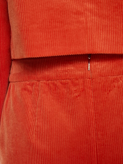 Frauenmodel trägt Minirock aus Cord mit Pattentaschen von Marc Cain in leuchtendem Orange, reine Baumwolle, Nahaufnahme Oberkörper.
