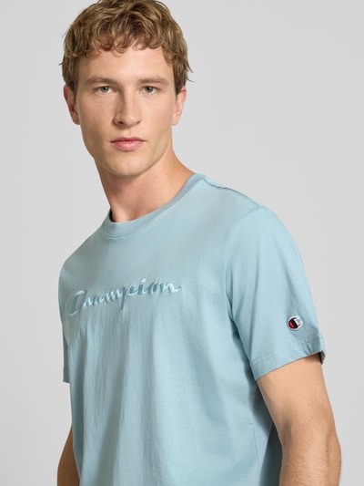 Männermodel trägt T-Shirt mit Label-Stitching mit Rundhalsausschnitt von CHAMPION in Hellblau, reine Baumwolle, Nahaufnahme Oberkörper.