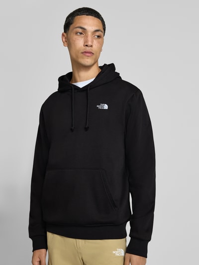 Männermodel trägt schwarzen Hoodie aus Baumwoll-Mix Modell 'EVOLUTION' von The North Face mit Känguru-Tasche, lockere Passform, Ganzkörperansicht von vorne.