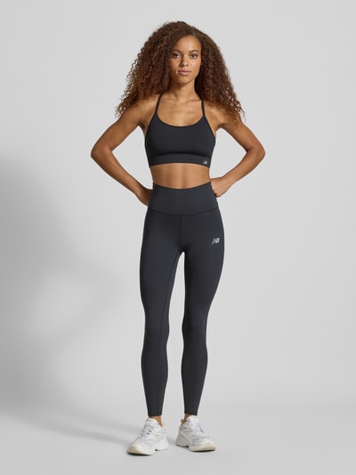 Frauenmodel trägt schwarze Leggings mit Label-Print Modell 'Harmony' von New Balance, elastisches Material, hoher Bund, Ganzkörperansicht von vorne.
