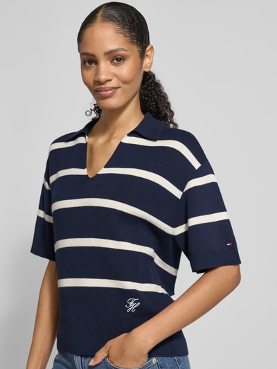 Frauenmodel trägt Regular Fit Pullover aus reiner Baumwolle von Tommy Hilfiger, dunkelblau mit weißen Streifen, Polokragen, V-Ausschnitt, Feinstrick, Logo-Stitching, kurzarm, gerippte Abschlüsse, Ganzkörperansicht von vorne.