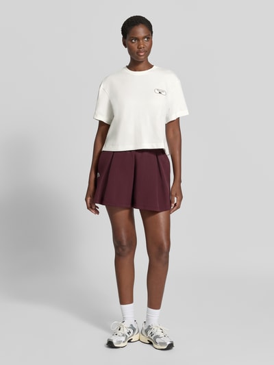 Vrouwenmodel draagt Regular Fit T-Shirt uit katoenmix van Lacoste in effen kleuren, korte lengte, labelprint en gestikt logo, jersey, ronde hals, korte mouw, look: effen, cropped, geheelvooraanzicht.
