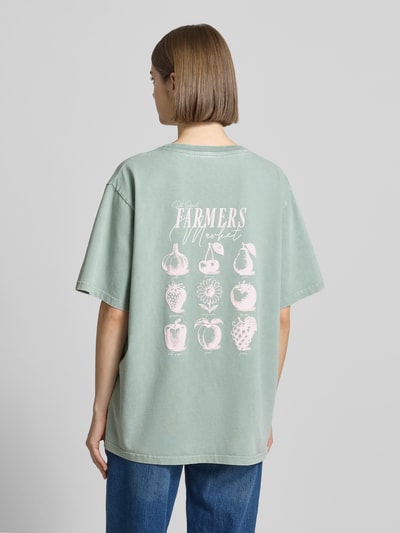 Frauenmodel trägt Damen T-Shirt von OH APRIL aus Reine Baumwolle im Oversized-Stil, Rückenlänge 69 cm, Label-Stitching, Modell 'Farmers Market', Ganzkörperansicht Rückansicht.