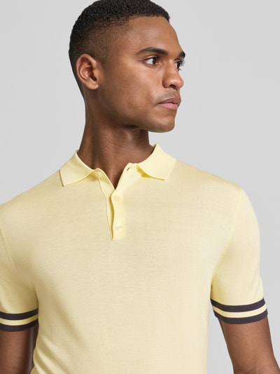 Męski model nosi Slim Fit Poloshirt aus Lyocell-Seide-Mix od Guess z kontrastowymi paskami, krój slim fit, polokragen, zbliżenie na górną część ciała.