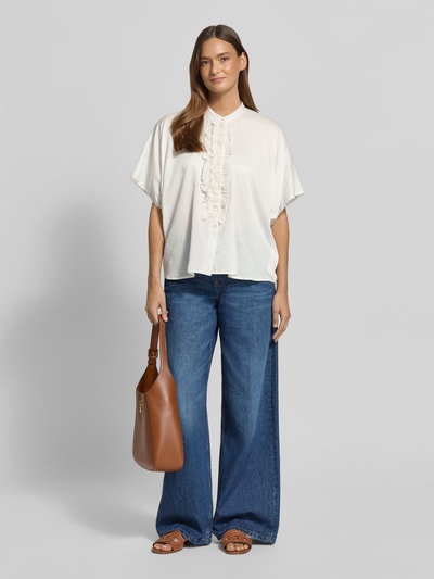 Frauenmodel trägt weiße Relaxed Fit Bluse mit Rüschen Modell 'DAISY' von 0039 Italy aus Baumwolle, kombiniert mit blauer Jeans, Ganzkörperansicht von vorne