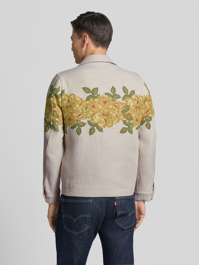 Männermodel trägt Strickjacke mit Kentkragen von Drykorn, Material-Mix mit Baumwoll-Anteil, helle Grundfarbe, florales gelb-grünes Muster, Gerader-Schnitt, Rückenlänge 70 cm, Schulterbreite 42 cm, Brustweite 67 cm, Ärmellänge 66 cm, Reißverschluss, Ganzkörperansicht Rückansicht.