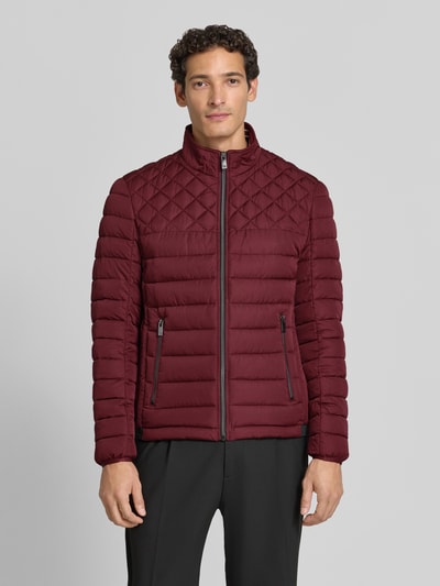 Männermodel trägt Steppjacke mit Stehkragen und Reißverschlusstaschen von Christian Berg Men in Dunkelrot, Ganzkörperansicht von vorne, Regular Fit, sichtbare Reißverschlüsse und gesteppte Textur, Kontext: Rückenlänge 68 cm, Schulterbreite 48 cm, Brustweite 60 cm, Ärmellänge 69 cm.