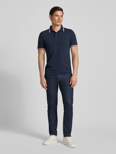 Männermodel trägt koszulkę polo Slim Fit Poloshirt mit Kontraststreifen Modell 'Brice' von Sundek, mieszanka bawełny i elastanu, krój slim fit, listwa guzikowa, paski w kontrastowym kolorze, długość tyłu w rozmiarze M: 70 cm, widok całej sylwetki z przodu.