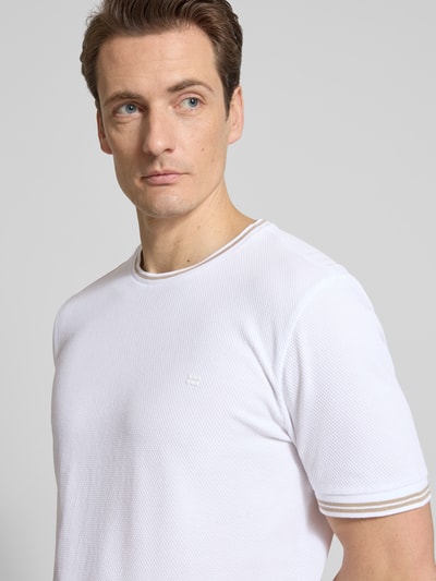 Męski model nosi T-shirt mit Strukturmuster und Rundhalsausschnitt von Christian Berg Men, mieszanka bawełny i elastanu, krój regular fit, fakturowany wzór, okrągły dekolt, długość tyłu w rozmiarze M: 70 cm, jasny kolor, delikatna faktura materiału, zbliżenie na górną część ciała, ujęcie z przodu.