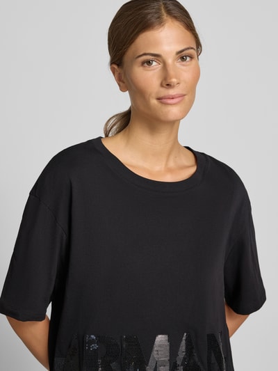 Vrouwenmodel draagt t-shirt met paillettenbesatz van Armani Exchange in zwart, puur katoen, losse pasvorm, ronde hals, labelprint; close-up bovenlichaam.