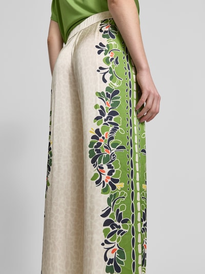 Frauenmodel trägt Wide Leg Pants aus Viskose-Mix mit Eingrifftaschen von Marc Cain, florales Muster, grün und beige, Detailaufnahme seitlich. Loose Fit, elastischer Bund, Stretch-Anteil, französische Eingrifftaschen, Bundweite 38 cm, Innenbeinlänge 77 cm bei Größe 36.