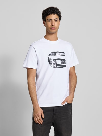 Männermodel trägt Regular Fit T-Shirt mit Logo-Print Modell 'icon' von G-Star Raw aus reiner Baumwolle, weiß mit schwarzem Print, Rundhalsausschnitt, Rückenlänge bei Größe M: 71 cm, Ganzkörperansicht von vorne.