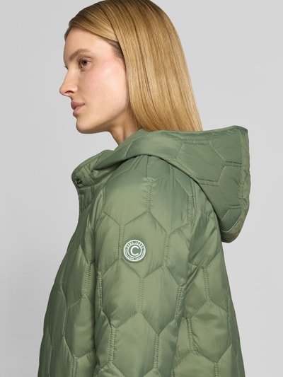 Frauenmodel trägt Regular Fit Mantel in Stepp-Optik Modell 'Solene' von CARS JEANS, olivgrün, Kapuze, Stehkragen, Eingrifftasche, Nahaufnahme Oberkörper. Rückenlänge 95 cm, Schulterbreite 42 cm, Brustweite 53 cm, Ärmellänge 47 cm bei Größe S.