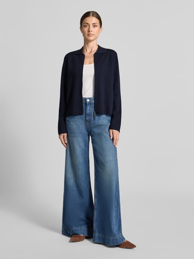 Frauenmodel trägt Strickjacke aus reiner Schurwolle Modell 'SNACK' von MM by Max Mara in Dunkelblau, Zweiwege-Reißverschluss, Ziernähte, lockere Passform, kombiniert mit heller Jeans, Ganzkörperansicht von vorne.