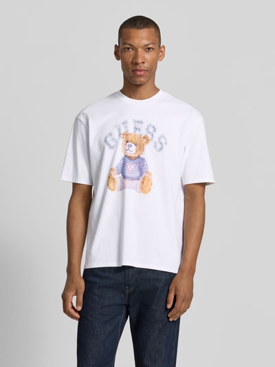 Männermodel trägt T-Shirt mit Motiv-Print und Rundhalsausschnitt von Guess aus Reine Baumwolle, Regular-Fit, Weiß, Ganzkörperansicht von vorne. Rückenlänge bei Größe M: 68 cm.
