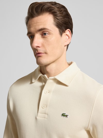 Męski model nosi Regular Fit Sweatshirt aus reiner Baumwolle od Lacoste, kremowy kolor, logo na piersi, krój regular fit, długi rękaw, materiał bawełniany, struktura prążkowana, z polokołnierzykiem, optyka jednolita/melange, naszywka z logo, zbliżenie na górną część ciała.