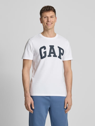 Männermodel trägt T-Shirt mit Logo und Rundhalsausschnitt von GAP aus reiner Baumwolle, Regular-Fit, weiß-blau, Ganzkörperansicht von vorne. Rückenlänge bei Größe M: 72 cm.