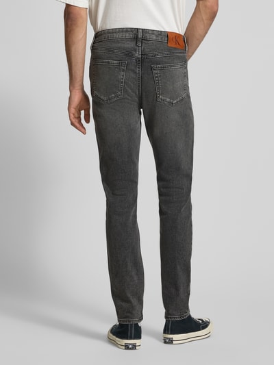 Männermodel trägt Slim Fit Jeans mit Label-Patch Modell 'HEARST' von Calvin Klein Jeans im Used-Look, Ganzkörperansicht Rückansicht.
