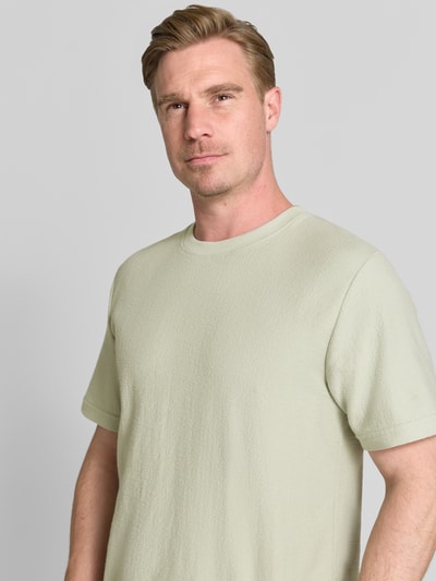 Männermodel trägt T-Shirt mit Rundhalsausschnitt Modell 'ODIN' von Samsøe Samsøe in Beige, Baumwoll-Mix, Regular-Fit, Label-Detail, Nahaufnahme Oberkörper. Herren T-Shirt, Rückenlänge bei Größe M: 70 cm.