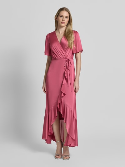 Frauenmodel trägt Abendkleid in Wickel-Optik mit Bindegürtel von Christian Berg Cocktail in Satin, taillierter Schnitt, Maxikleid, V-Ausschnitt, Volantsaum, in Rosa, Ganzkörperansicht von vorne.