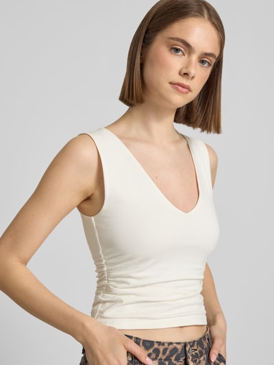 Modelka kobieca nosi Slim Fit Trägertop mit Raffungen und V-Ausschnitt Modell 'MY' od Topshop, bawełna z elastanem, krój slim fit, cropped, dekolt V, marszczenia, długość pleców w rozmiarze S: 43 cm, jasny kolor, lekka tekstura, zbliżenie na górną część ciała z przodu