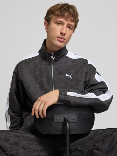 Männermodel trägt Trainingsjacke mit Reißverschluss und Logo von PUMA PERFORMANCE in Schwarz mit Weiß, Relaxed-Fit, Nahaufnahme Oberkörper.