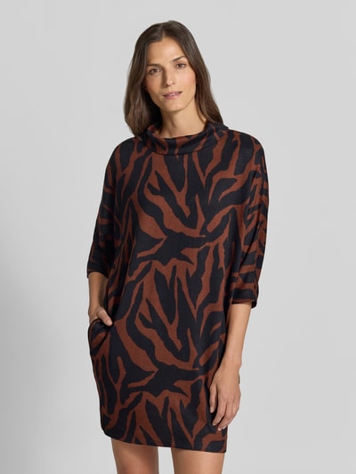 Frauenmodel trägt Minikleid mit seitlichen Eingrifftaschen von Apricot, Material-Mix mit Stretch-Anteil, weiter Rollkragen, 3/4-Arm, braun-schwarzes Muster, Straight Fit, Ganzkörperansicht von vorne.