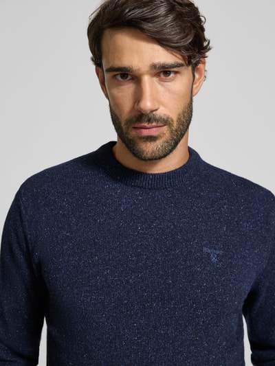 Männermodel trägt Pullover aus Woll-Seide-Mix mit Rundhalsausschnitt Modell 'TISBURY' von BARBOUR in Dunkelblau, Nahaufnahme Oberkörper. Unifarbene Stricktextur mit geripptem Abschluss, dezentes Markenlogo, Herrenmode.
