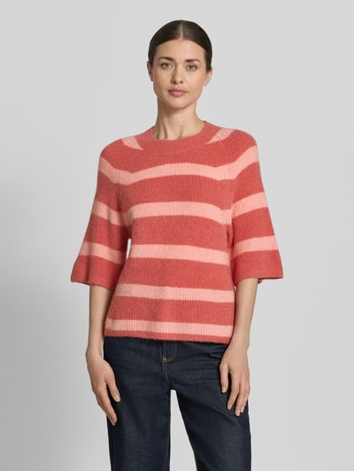 Frauenmodel trägt Strickpullover mit 1/2-Arm Modell 'Milania Hope' von MSCH Copenhagen, Material-Mix mit Alpaka-Anteil, Gerader-Schnitt, Rundhalsausschnitt, Streifen in Rosa- und Koralltönen vor grauem Hintergrund, Ganzkörperansicht von vorne.