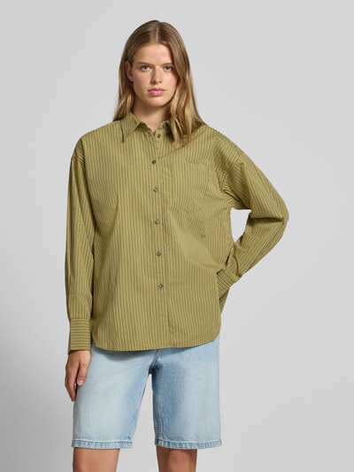 Frauenmodel trägt Relaxed Fit Hemdbluse aus reiner Baumwolle Modell 'JAMIE' von JJXX mit feinen Streifen, Hemdblusenkragen, Brusttasche, Knopfleiste und überschnittenen Schultern, kombiniert mit hellblauer Jeansshorts, Farbkombination aus Grün und Gelb, glatte Textur, Ganzkörperansicht von vorne.