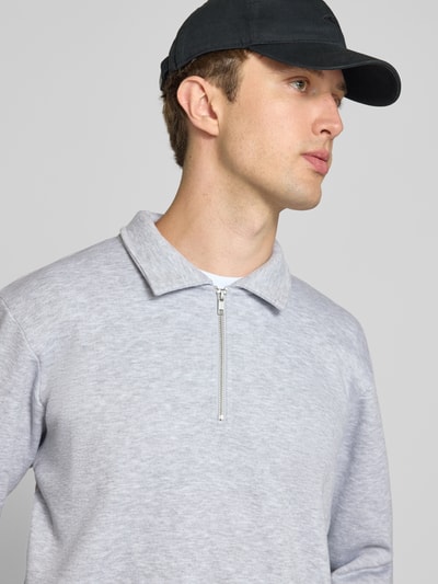 Männermodel trägt Regular Fit Sweatshirt mit Baumwoll-Anteil Modell 'Bradley' von JACK & JONES in Hellgrau, Nahaufnahme Oberkörper. Material-Mix, Troyer-Kragen, Reißverschluss, Rückenlänge 69 cm bei Größe M.