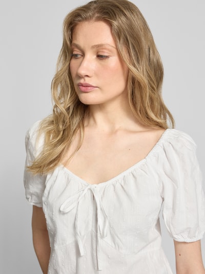 Frauenmodel trägt A-Linien Umstandskleid aus reiner Baumwolle Modell 'JUTTY' von Vero Moda, weiß, Ballonärmel, Strukturmuster, Nahaufnahme Oberkörper.
