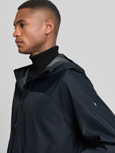 Männermodel trägt Regular Fit Mantel mit Logo-Detail Modell 'Treeline' von Peak Performance in Schwarz, Nahaufnahme Oberkörper. Rückenlänge 97 cm, Schulterbreite 46 cm, Brustweite 60 cm, Ärmellänge 66 cm, Kapuze mit Stehkragen, Zweiwege-Reißverschluss, Eingrifftaschen, geeignet als Herren Mantel.