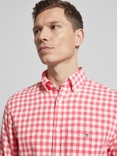 Männermodel trägt Regular Fit Leinenhemd mit Baumwoll-Anteil Modell 'GINGHAM' von Gant, rot-weiß kariert, Nahaufnahme Oberkörper. Leinen-Baumwoll-Mix, Button-Down-Kragen, Brusttasche mit Label-Stitching.
