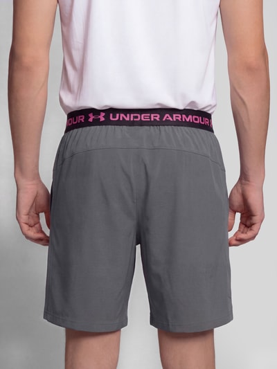Männermodel trägt graue Regular Fit Sportshorts mit Logo-Print von Under Armour, elastischer Bund in Schwarz und Pink, Ganzkörperansicht Rückansicht. Herren Sportshorts von Under Armour