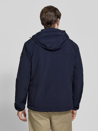 Männermodel trägt Jacke mit Label-Print Modell 'TUNDRA' von Napapijri in Dunkelblau, strukturierte Oberfläche, Ganzkörperansicht Rückansicht. Gerade Passform, Kapuze mit Tunnelzug, Logo-Patch am Ärmel, durchgehender Reißverschluss, Reißverschlusstaschen, elastische Ärmelabschlüsse, Rückenlänge 72 cm, Schulterbreite 48 cm, Brustweite 55 cm, Ärmellänge 63 cm.
